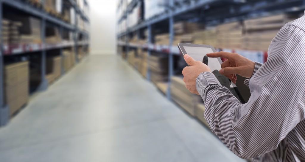 Businessman working on logistic inside stock room with touchscreen tablet.