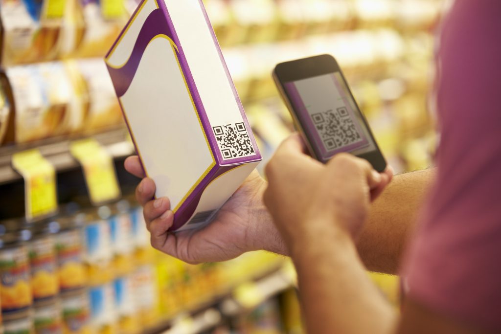 Man Scanning QR Code In Supermarket With Mobile Phone