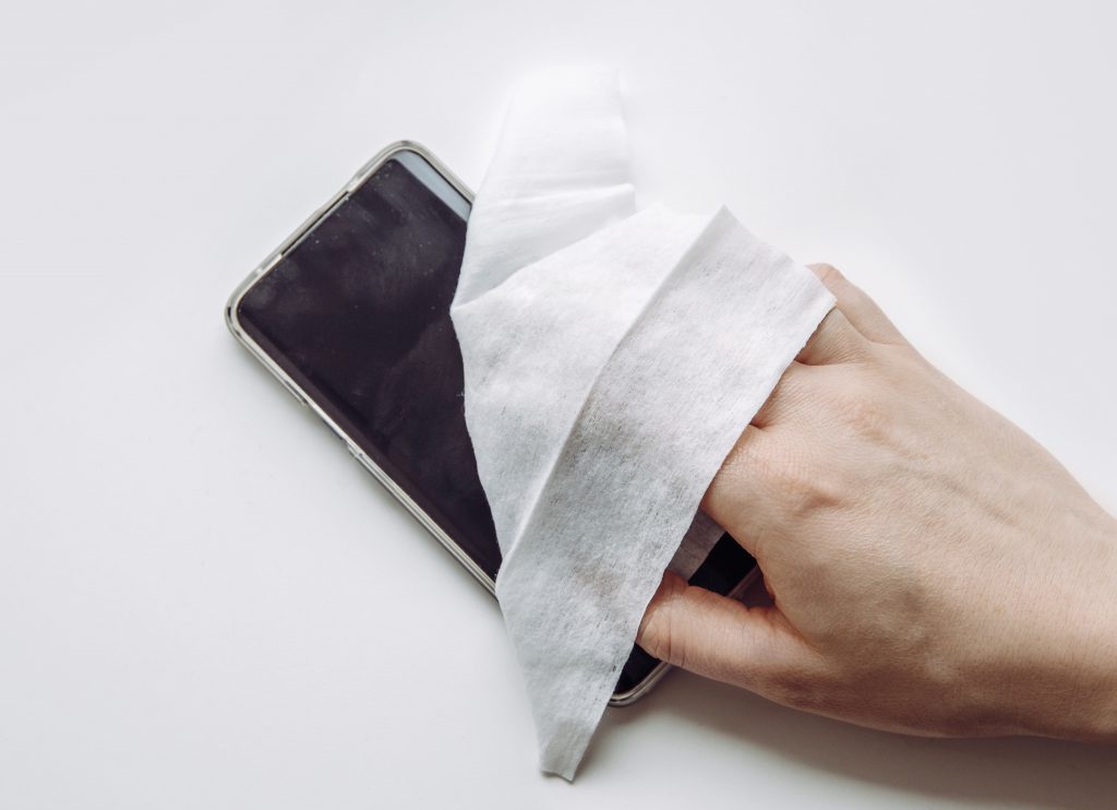 Close up view of man hand using antibacterial wet wipe for disinfecting smartphone touch screen.