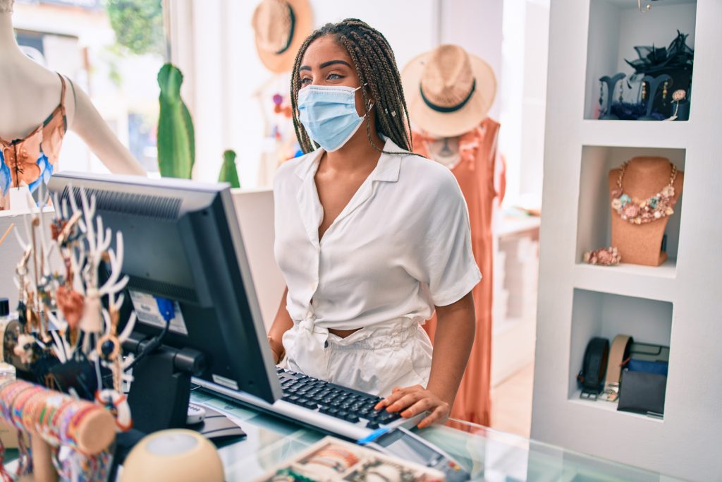 Woman smiling happy working at the till wearing coronavirus safety mask at retail shop