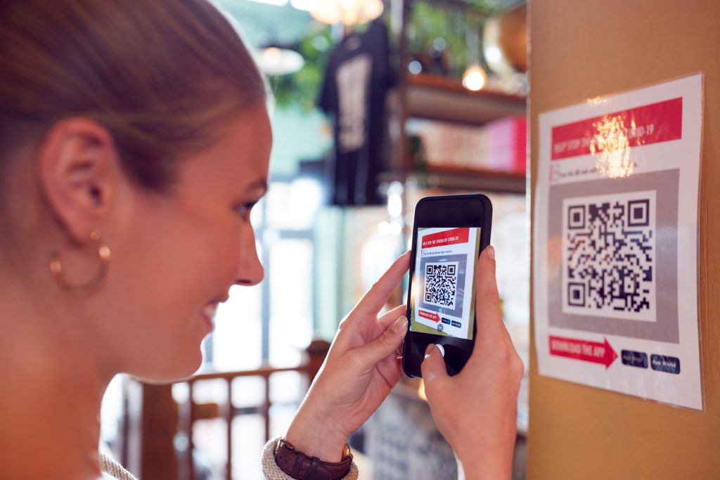 Woman With Mobile Phone Checking Into Venue Scanning QR Code During Health Pandemic