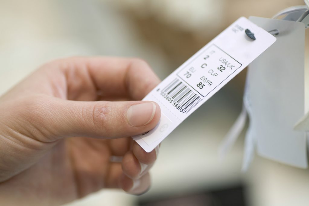 Someone holding a tag with a barcode on clothing in a retail store